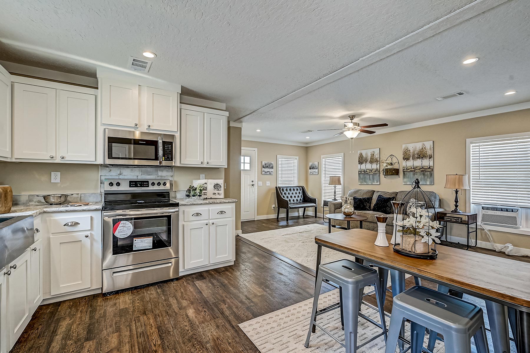 Modern open-plan kitchen and living area with white cabinets, stainless steel appliances, and wood flooring. Cozy seating with neutral tones adds a warm feel.