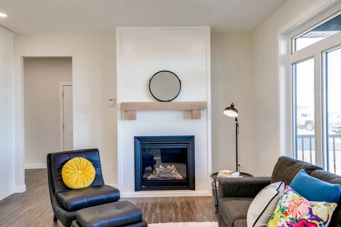 Modern living room with a cozy ambiance featuring a black leather chair with a yellow cushion, a sleek fireplace, and a gray sofa adorned with colorful pillows.