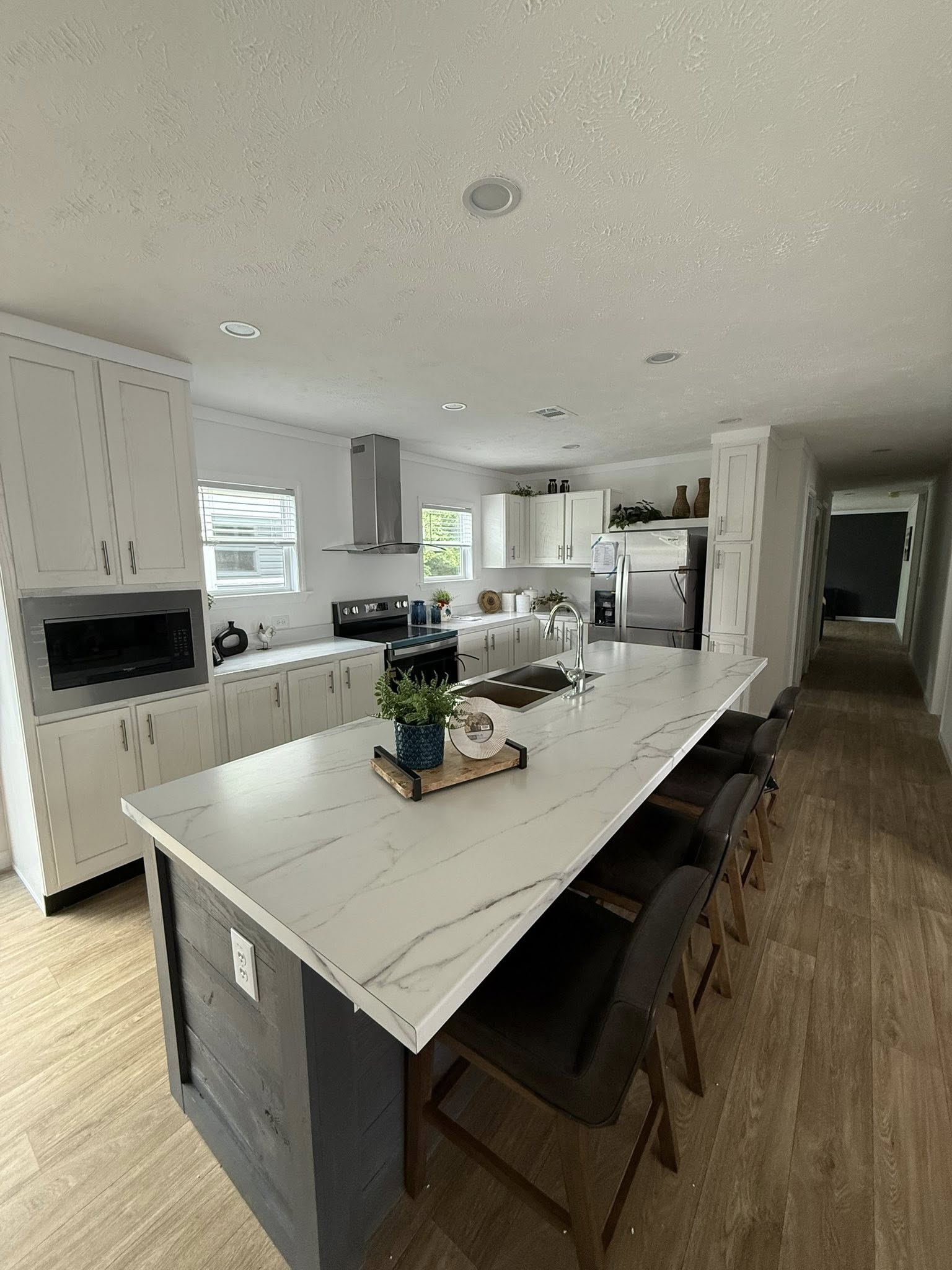 Modern kitchen with a long marble island, bar stools, and sleek appliances. White cabinets and wood flooring offer a clean, contemporary feel.