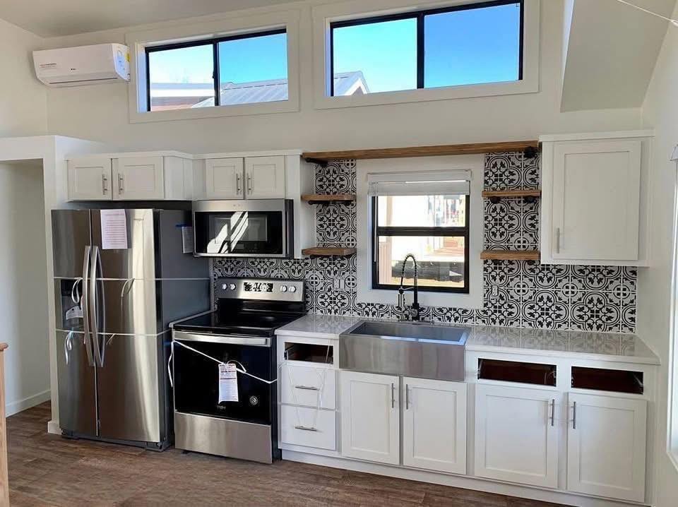 Modern kitchen with stainless steel appliances including a fridge and oven. White cabinets, patterned tile backsplash, and farmhouse sink. Bright and airy atmosphere.
