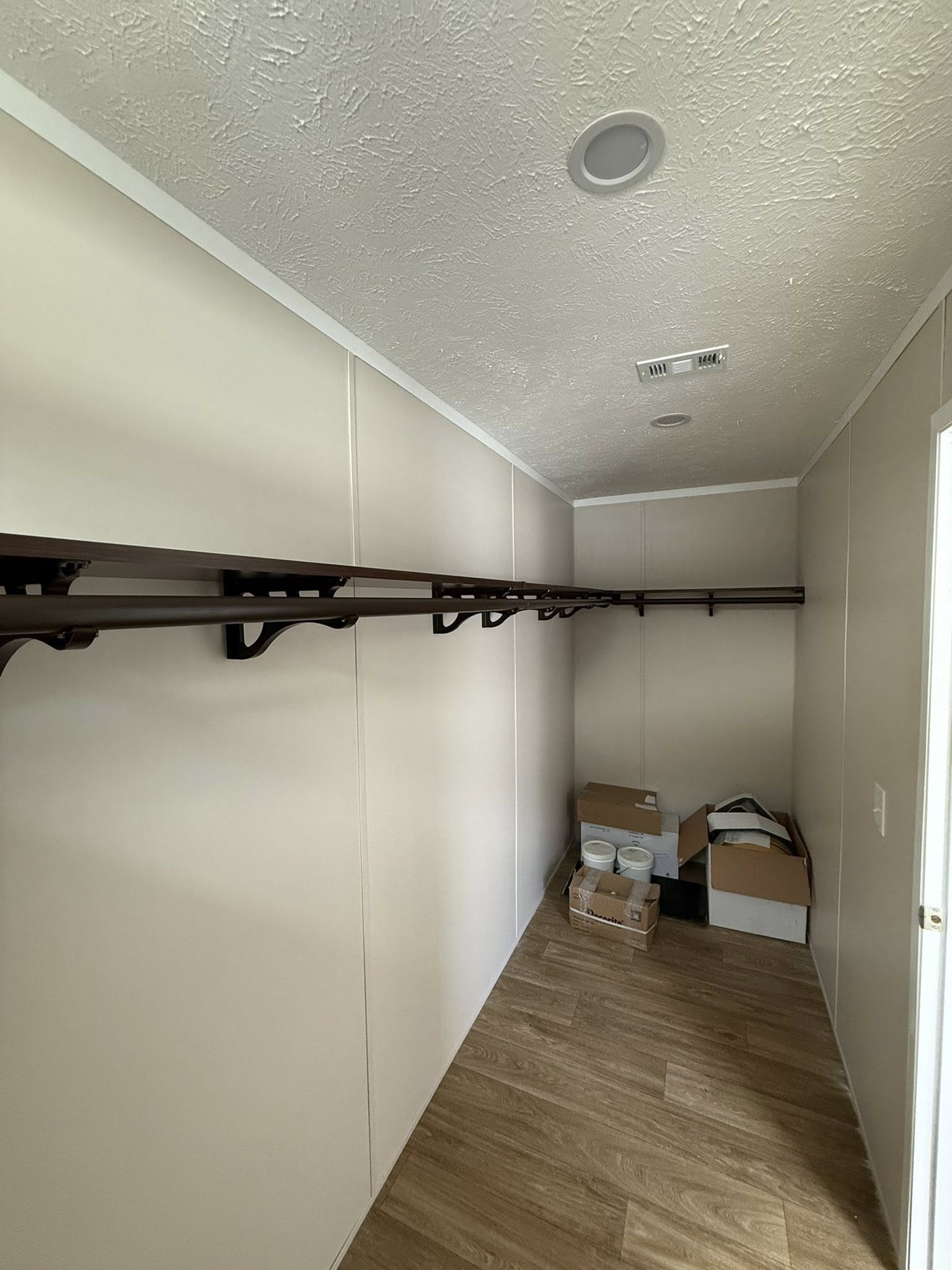 A minimalist bathroom features light wood flooring, a white toilet on the left, and an adjacent open door revealing an empty closet with a shelf.