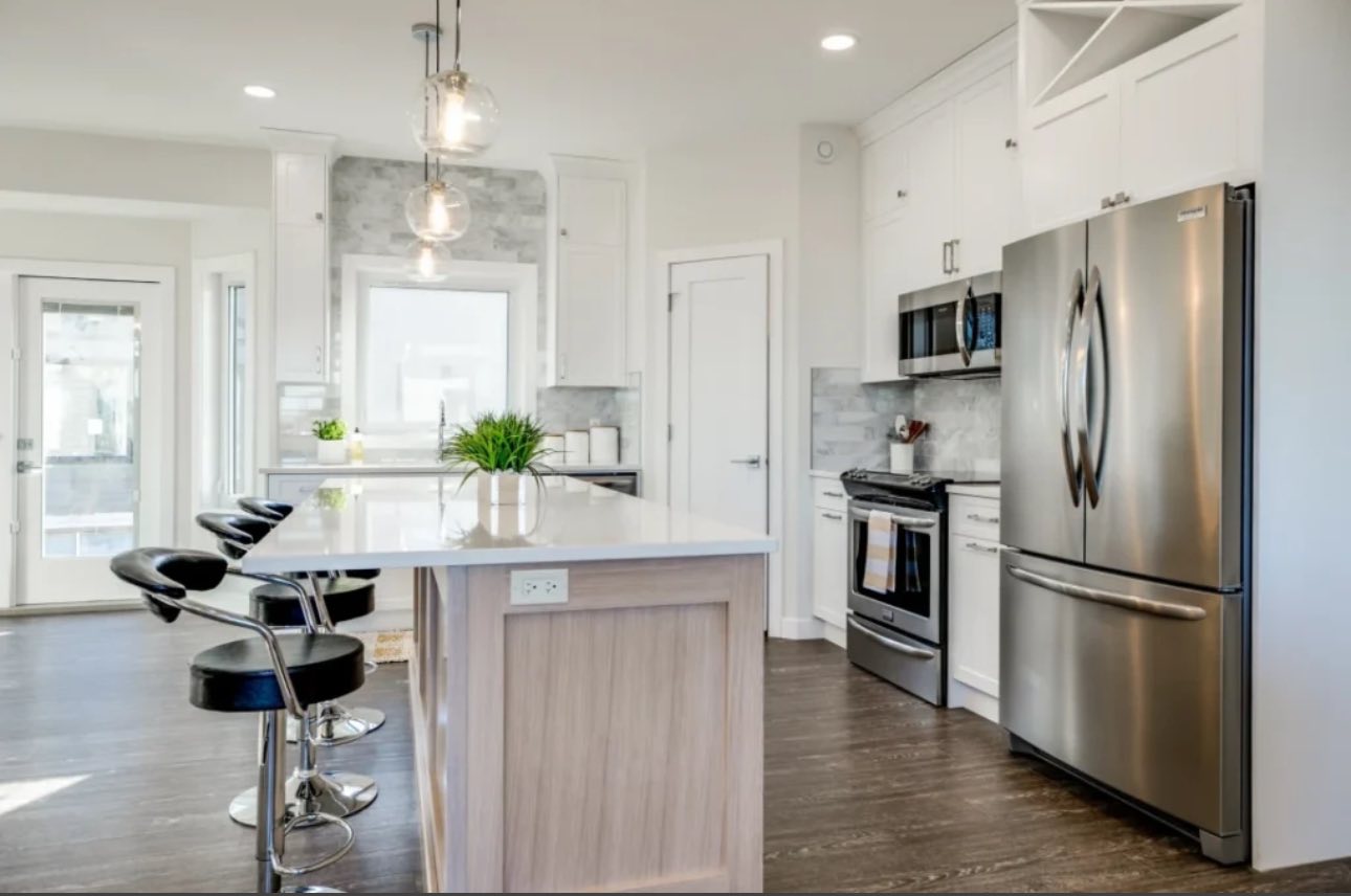 Modern kitchen with white cabinets, stainless steel appliances, and a central island. Three black bar stools align along the island, creating a sleek and inviting atmosphere.