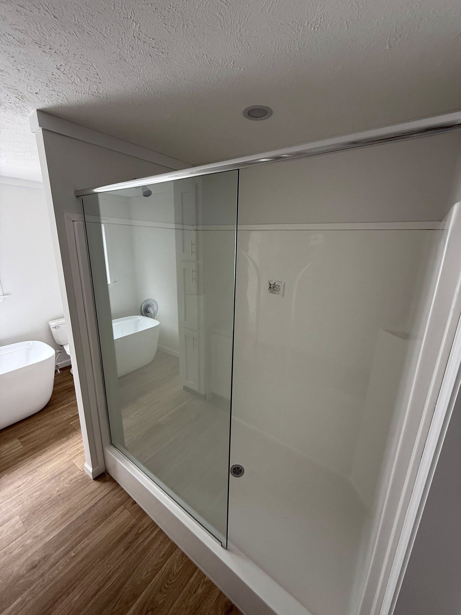 Modern bathroom with a wooden floor features a glass-enclosed shower. A sleek, white bathtub and toilet are visible in the background, creating a clean, minimalist vibe.