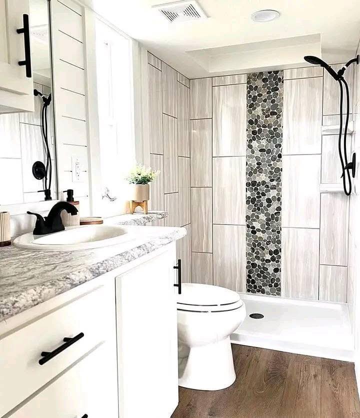 Modern bathroom with a white vanity and marble countertop, featuring a black faucet. The shower has a stone accent wall and sleek black fixtures, and there's a small plant on the counter.