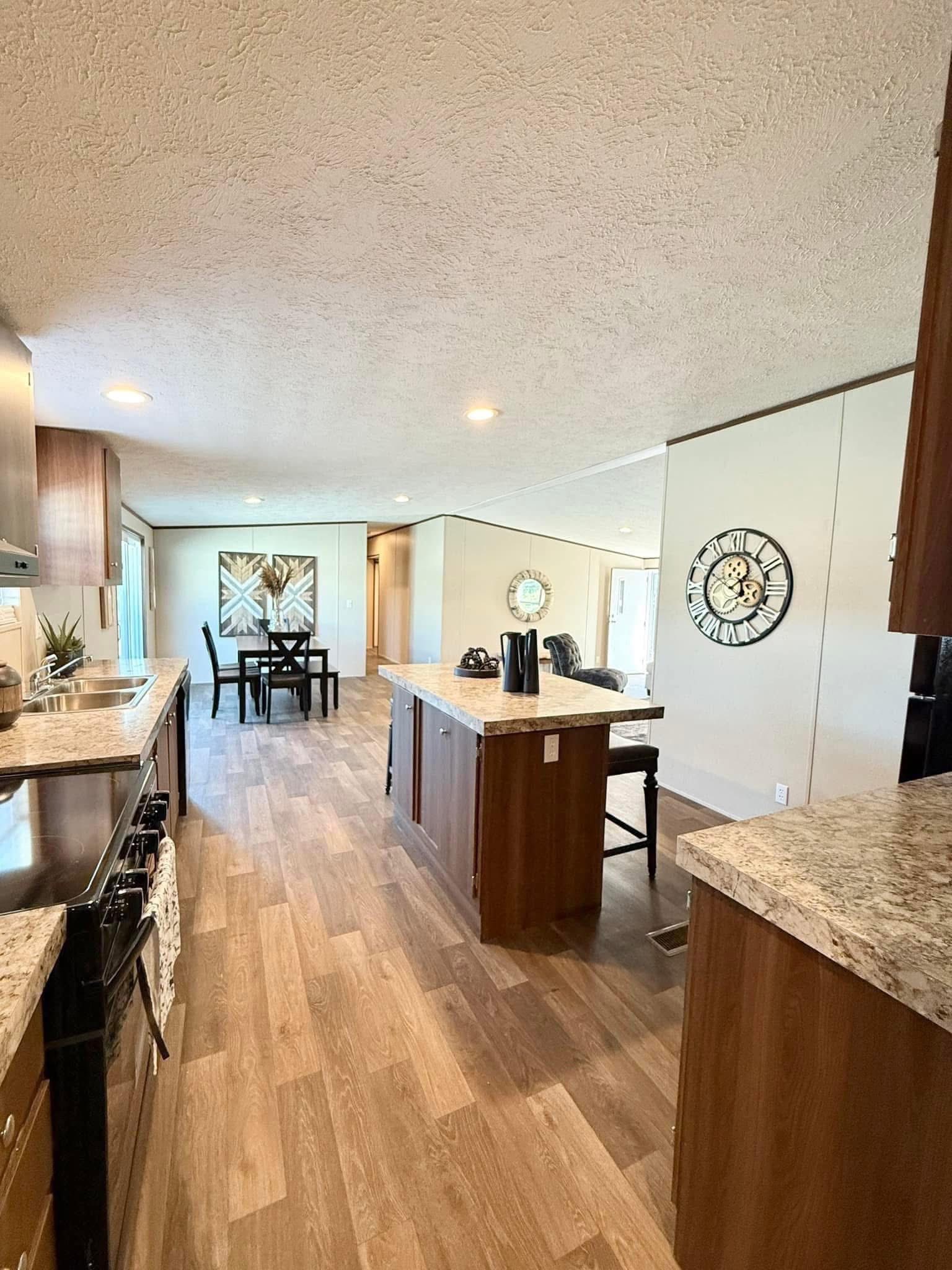 Spacious kitchen and dining area with wood floors, marble countertops, and modern decor. Wall clock and abstract painting add elegance and warmth.