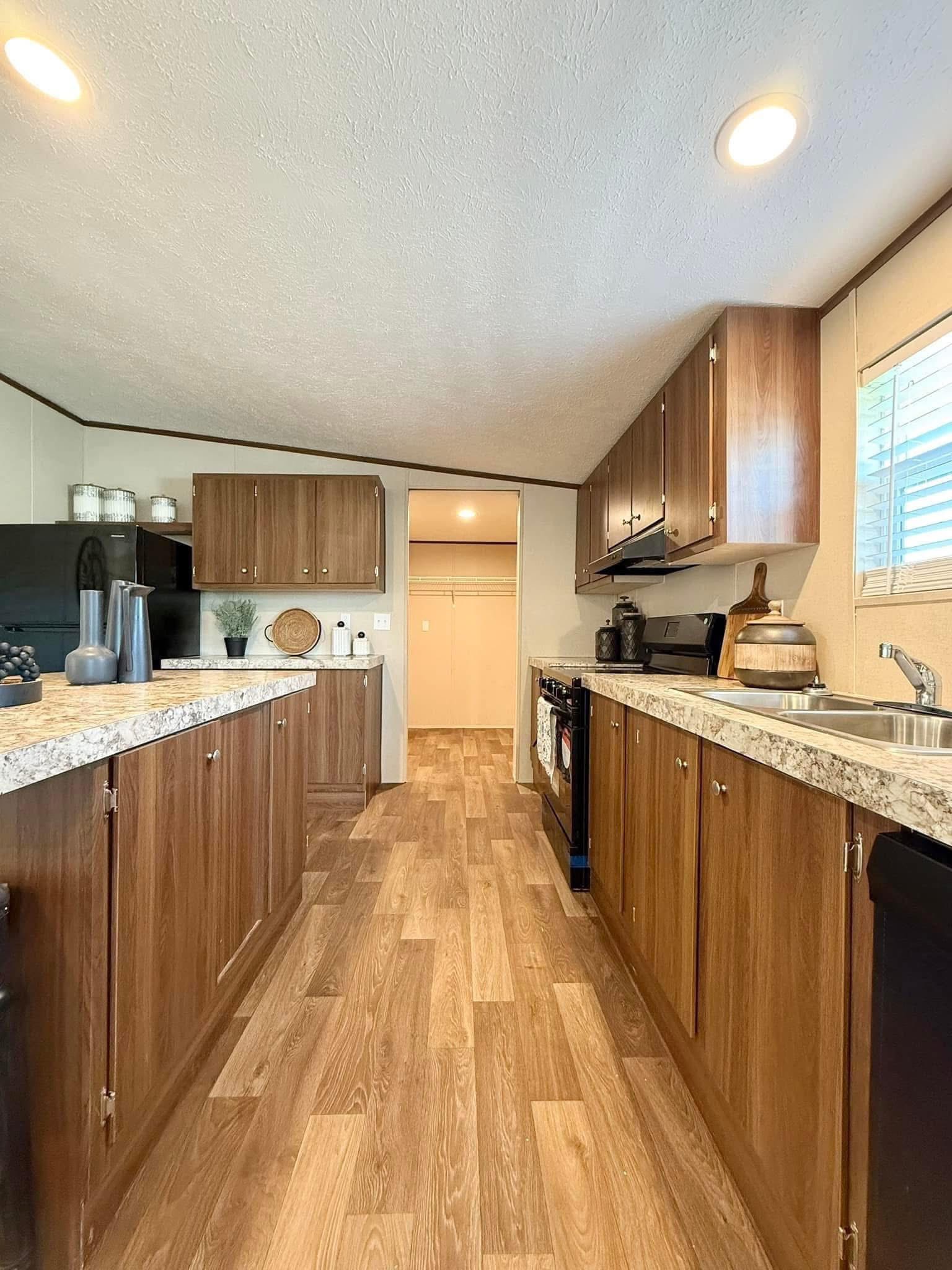 Sleek kitchen with wooden cabinets, marble countertops, and stainless steel appliances. Bright ceiling lights illuminate the space, providing a warm tone.