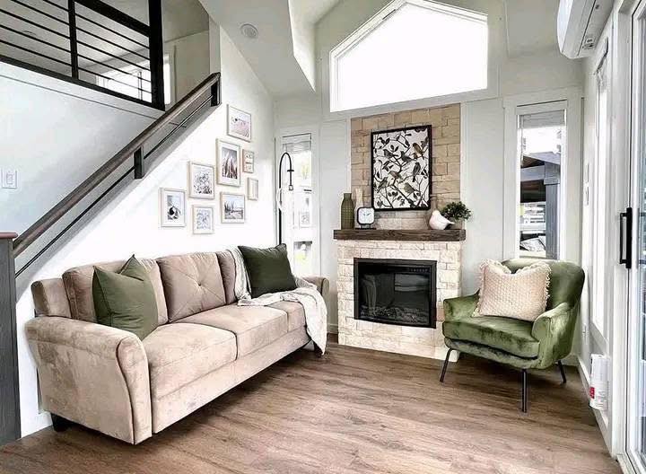 Cozy living room with a beige couch, green armchair, and a modern fireplace. Gallery wall, soft lighting, and wood flooring create a warm, inviting atmosphere.