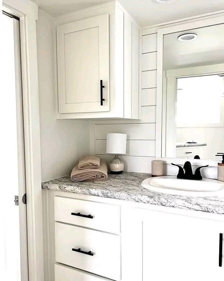 A modern bathroom features white cabinetry with black handles, a marble countertop, folded beige towels, and a sleek black faucet.
