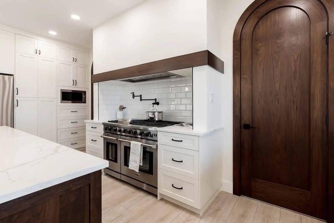 Sleek kitchen with stainless steel stove, white cabinetry, and subway tile backsplash. Large wooden arched door adds elegance and warmth.