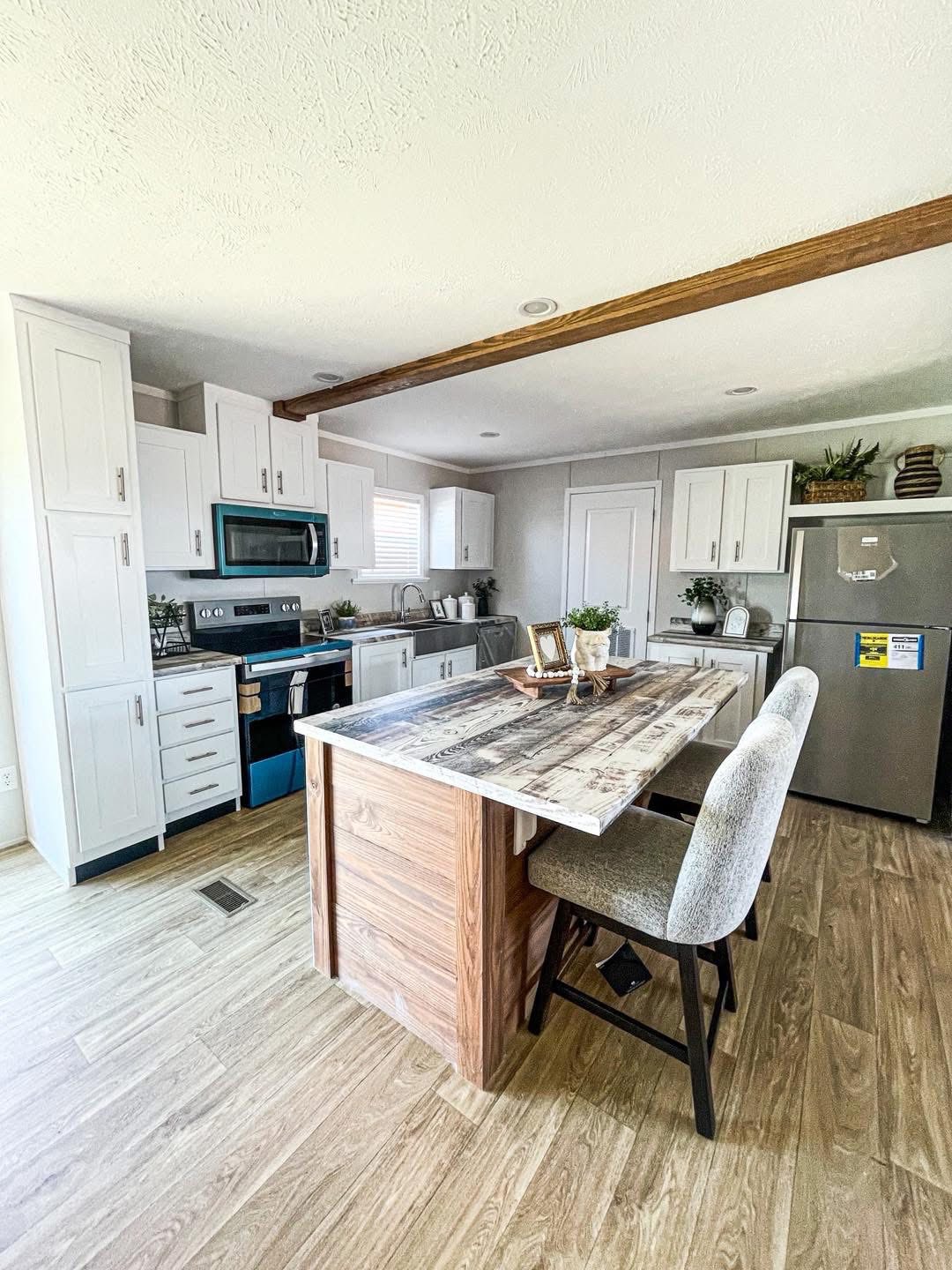Bright living room with beige sofas and floral cushions. A wooden coffee table with greenery sits on a gray patterned rug. Ceiling fan above. Airy, serene feel.