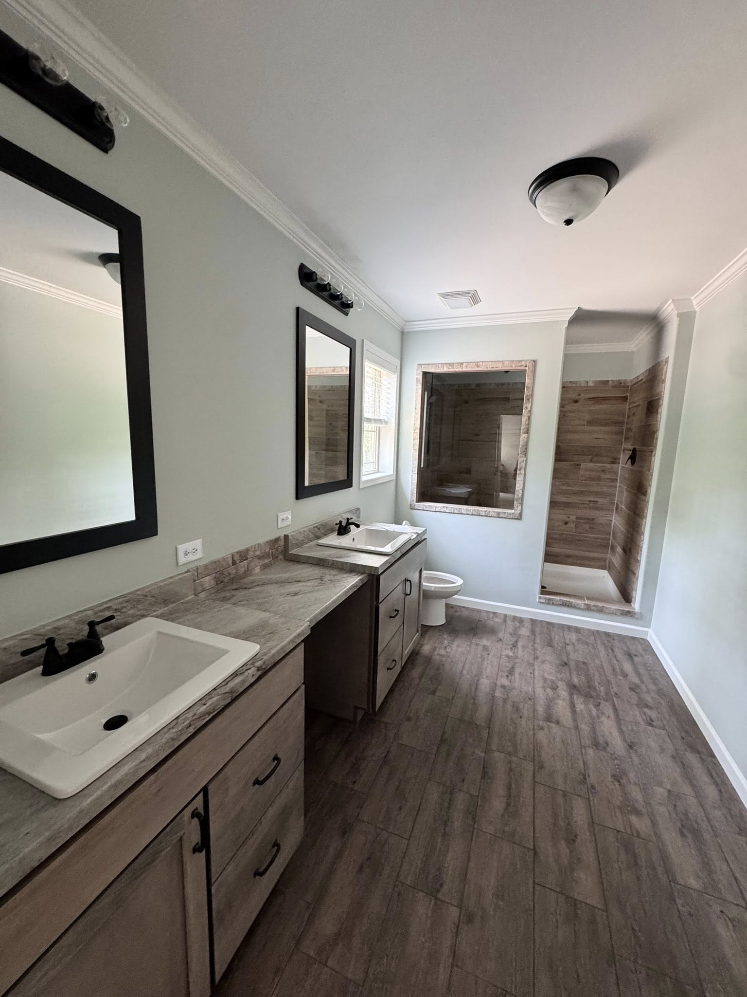 A modern bathroom with dual sinks on a wooden vanity, black-framed mirrors, and a wood-tiled shower. Neutral tones convey a calm, contemporary feel.