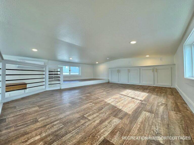A cozy loft space with wood flooring, white cabinets, and recessed lighting. Sunlight streams through a window, creating a warm and inviting atmosphere.