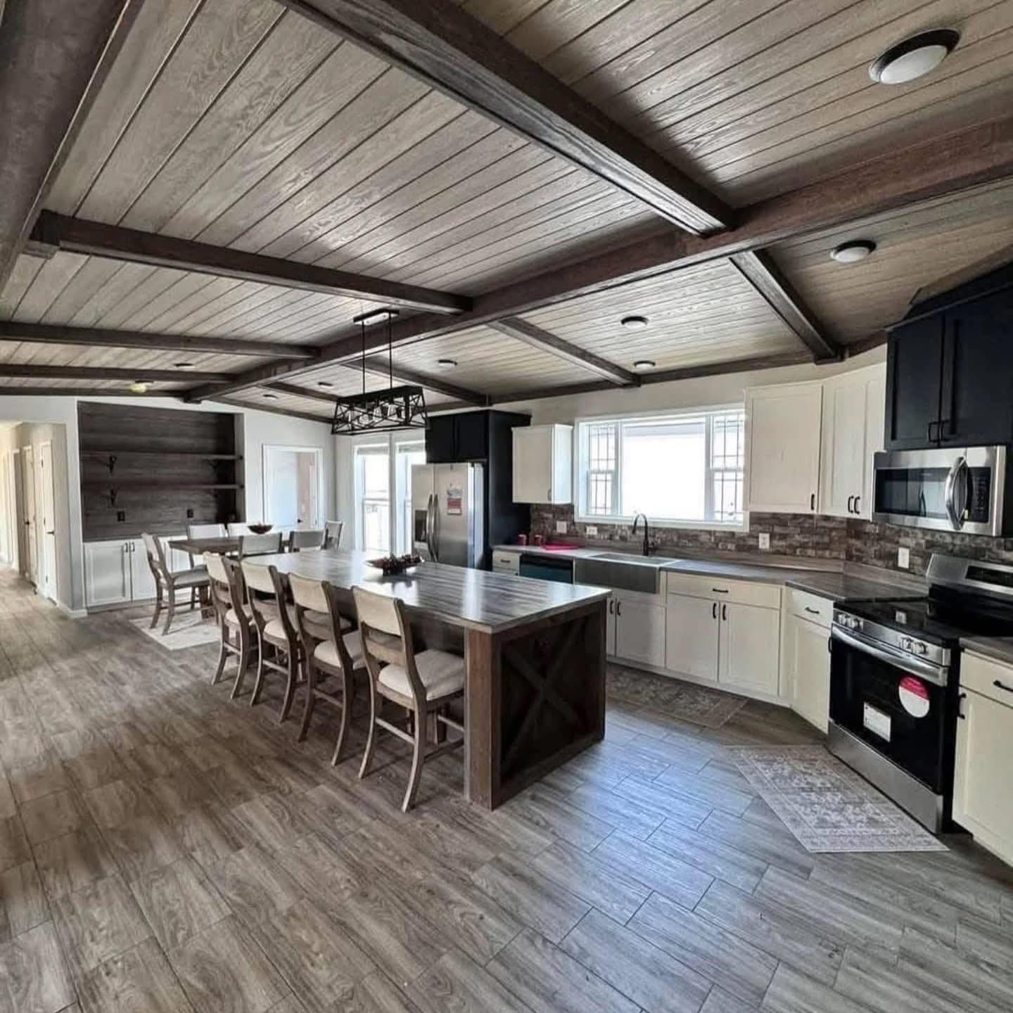 Spacious kitchen with rustic wood beams, large island seating six, white cabinets, stainless steel appliances, and a warm, inviting atmosphere.