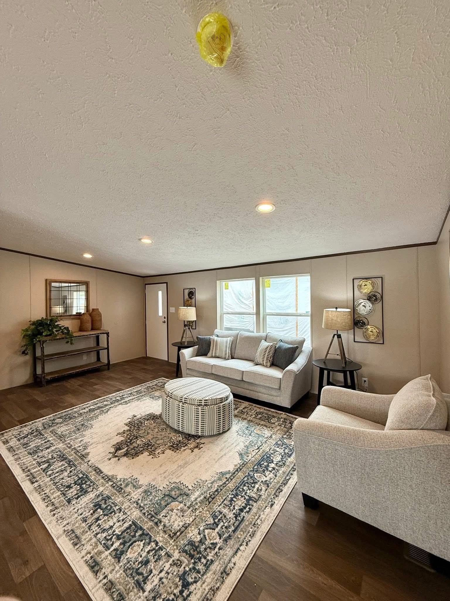 Spacious living room with a white sofa and armchair on a patterned rug. Warm lighting, wall art, and a potted plant create a cozy atmosphere.