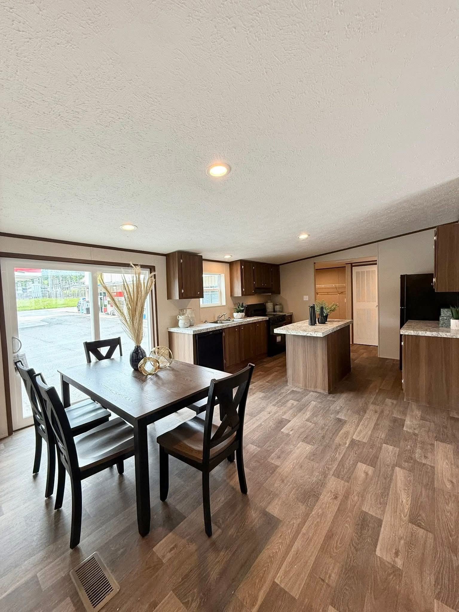 Spacious open-plan kitchen and dining area with wood flooring. Dark wood table, chairs, and elegant decor on the table. Bright, modern ambiance.