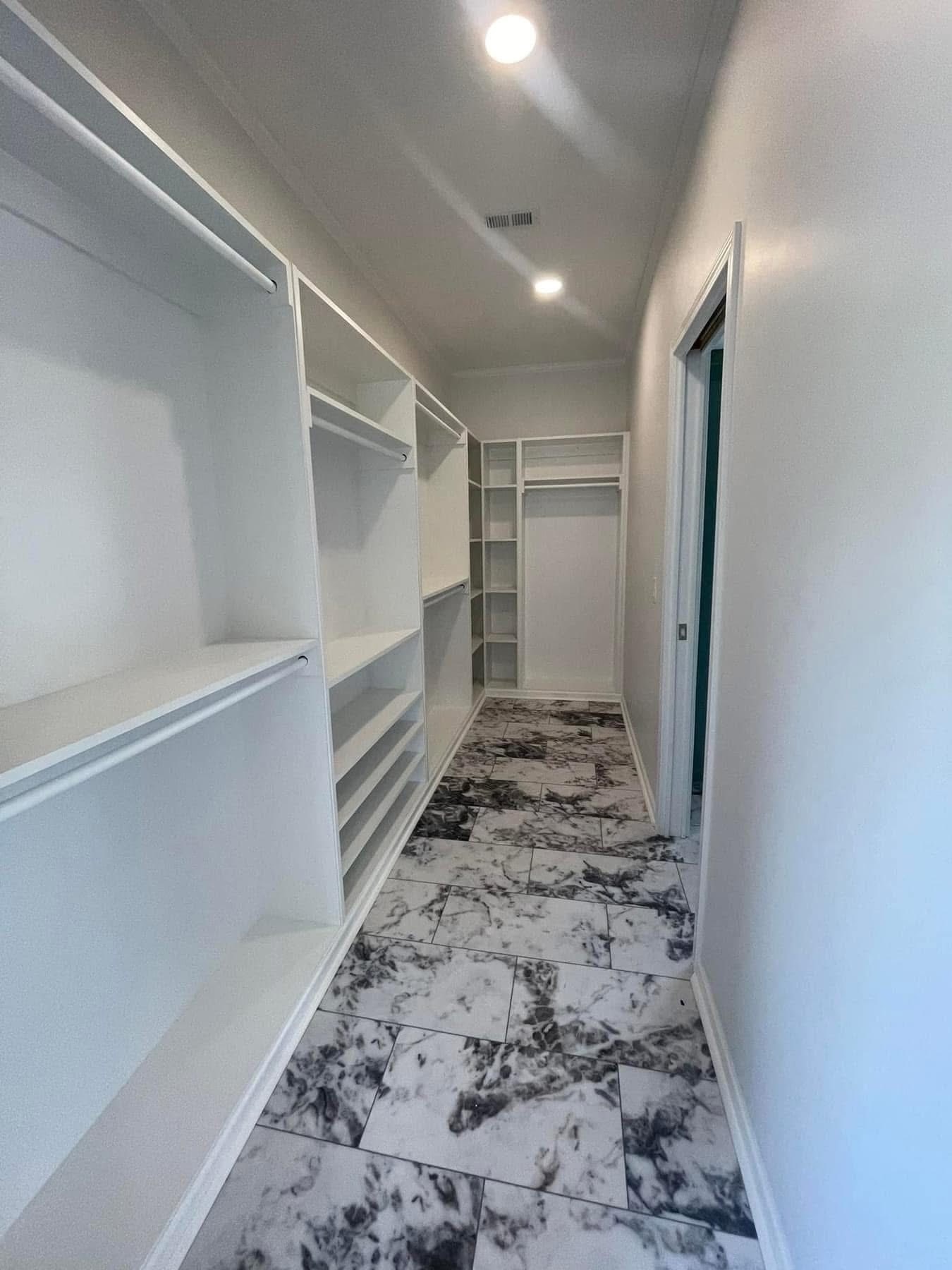 Narrow walk-in closet with white shelves on both sides, featuring a stylish black and white marble-patterned tile floor and a contemporary, minimalist design.