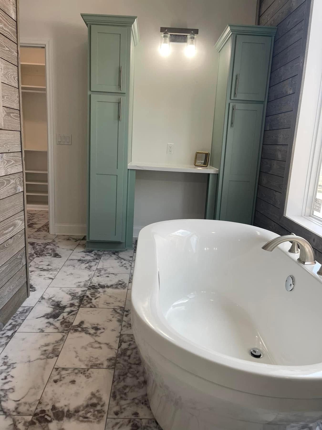 Luxurious bathroom with a large white bathtub, marble-patterned floor tiles, light green cabinets, and soft lighting, creating a serene atmosphere.
