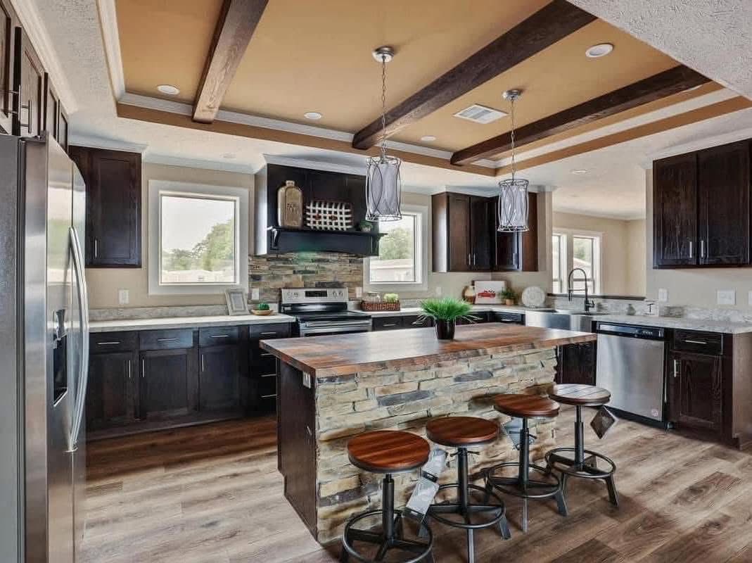 Modern kitchen with dark wood cabinets, stainless steel appliances, and a central island with stone accents. Warm lighting creates a cozy atmosphere.