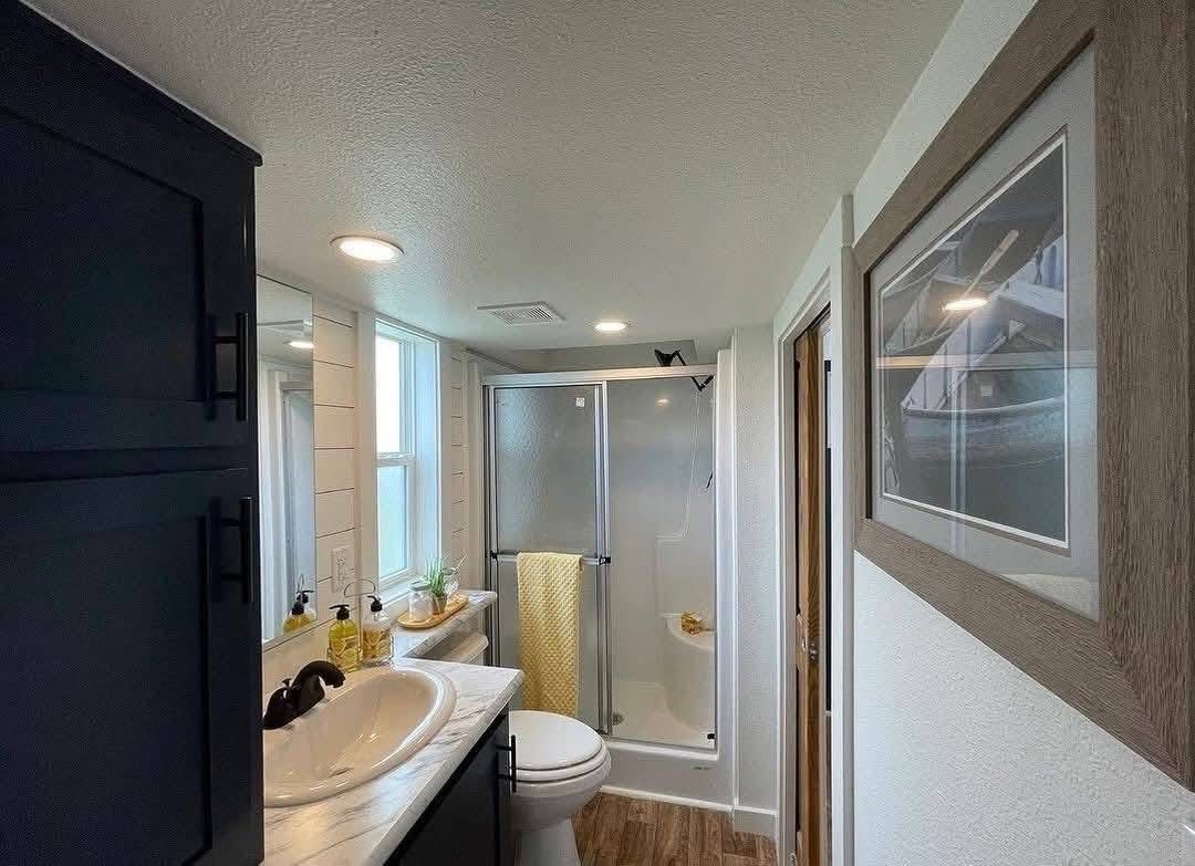 Modern bathroom with a glass shower, white sink, and wooden floor. A yellow towel adds a pop of color. Bright and clean aesthetic.