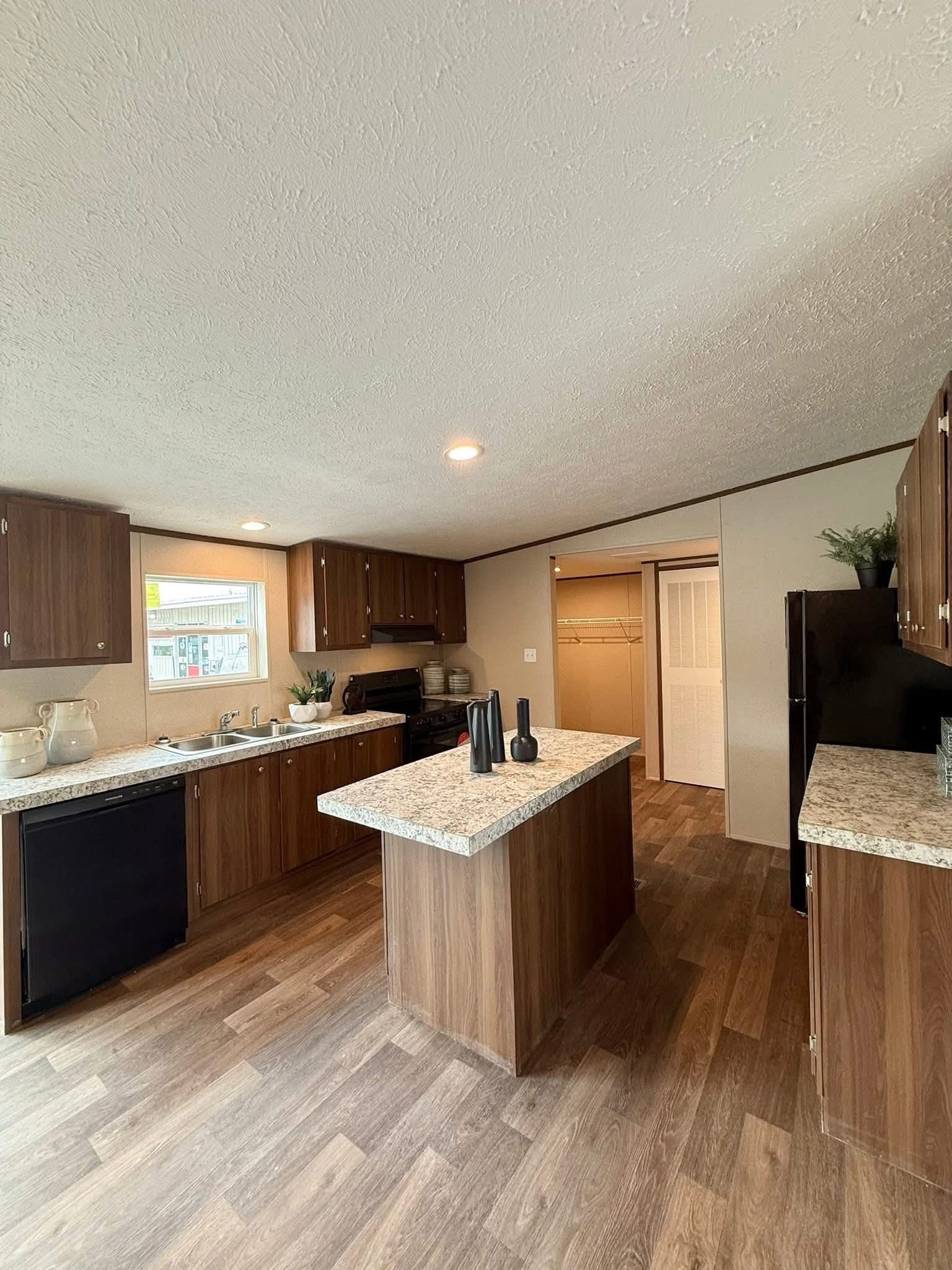 Modern kitchen with wood cabinets, marble countertops, and a central island. Black appliances and cozy lighting create a warm, welcoming atmosphere.