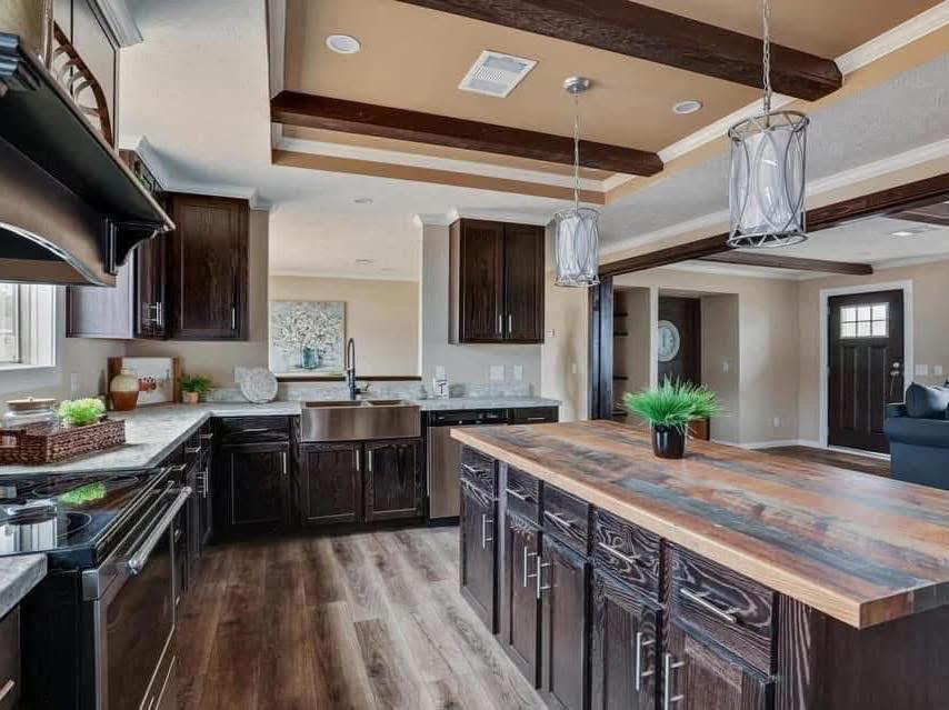 Modern kitchen with dark wood cabinets, a farmhouse sink, and a wooden island. Pendant lights hang above, and green plants add a fresh touch. Warm, inviting tones.