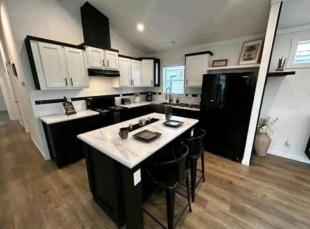 Modern kitchen with a black and white color scheme, featuring shaker cabinets, a central island with bar stools, and wooden floors. Cozy and stylish ambiance.