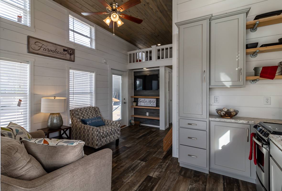 Cozy farmhouse-style interior with white shiplap walls and wooden floors. Features a loft, gray cabinets, and a mix of modern and rustic decor.