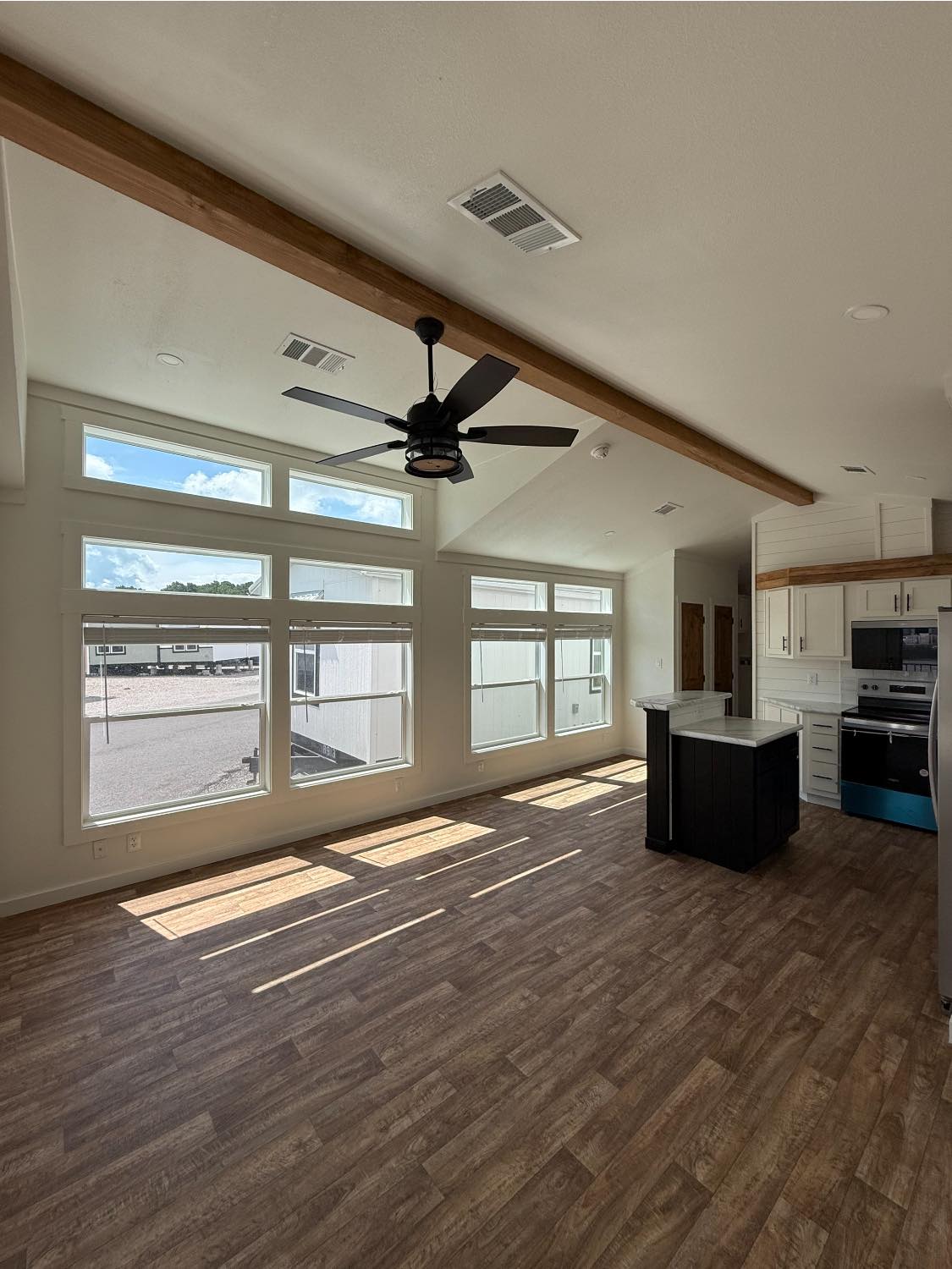 Bright, open-plan kitchen and living area with large windows, wood flooring, vaulted ceiling, wood beam, and modern appliances, conveying a spacious feel.