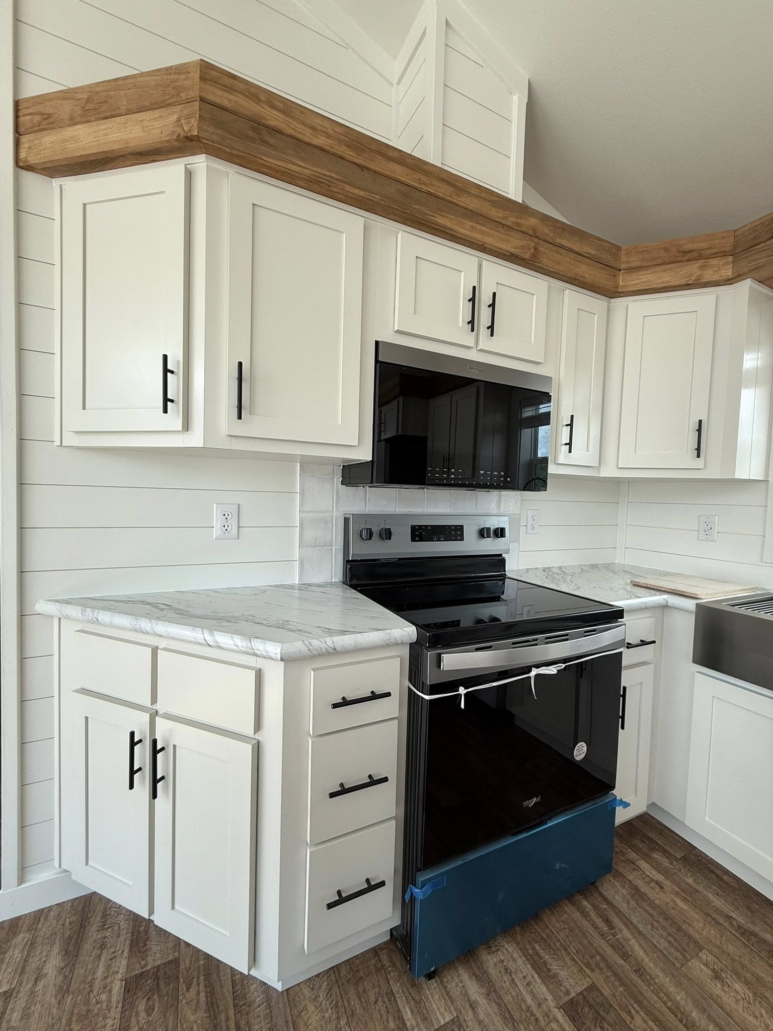 Modern kitchen with white shaker cabinets, black handles, and marbled countertops. Features a stainless steel oven and wood laminate flooring.