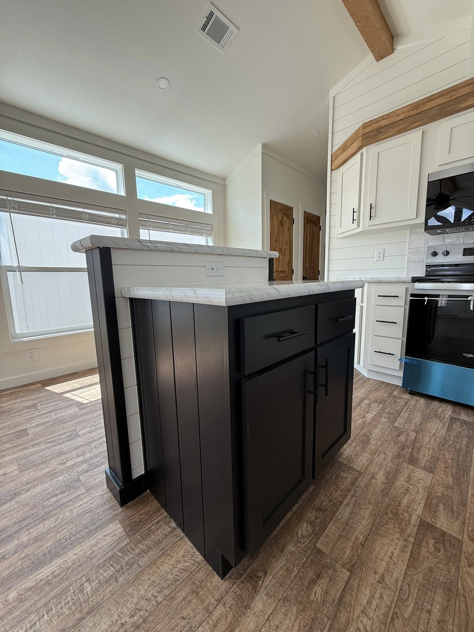 Modern kitchen with dark island, white countertops, light wood flooring, and large windows. Bright and airy with a cozy, inviting feel.