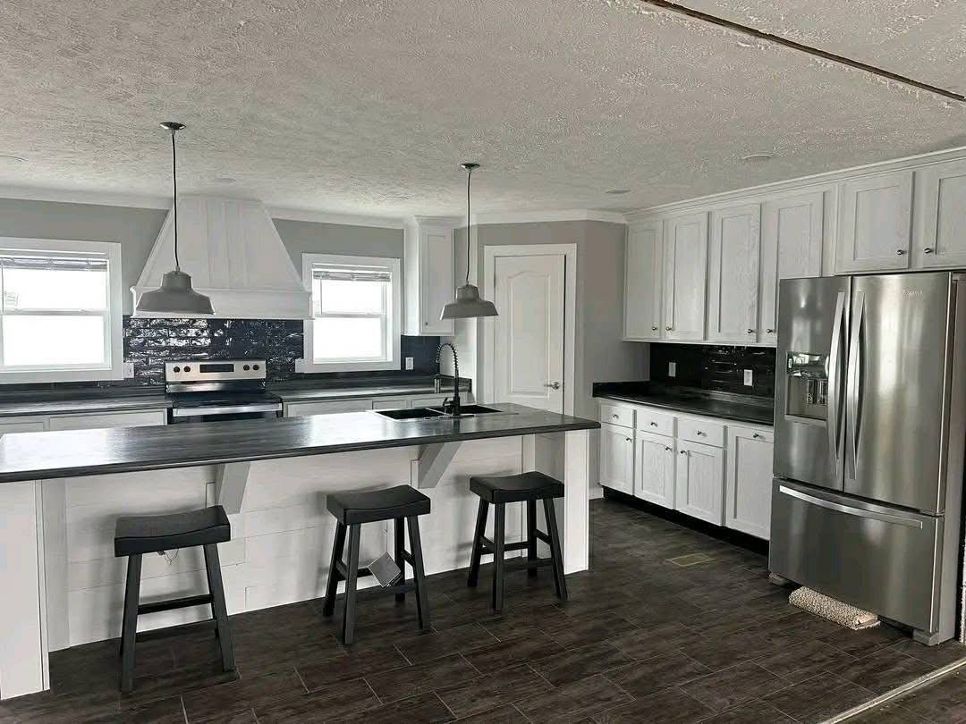 Modern kitchen with white cabinets, black countertops, and two pendant lights. Features a large island with three stools and stainless steel appliances.