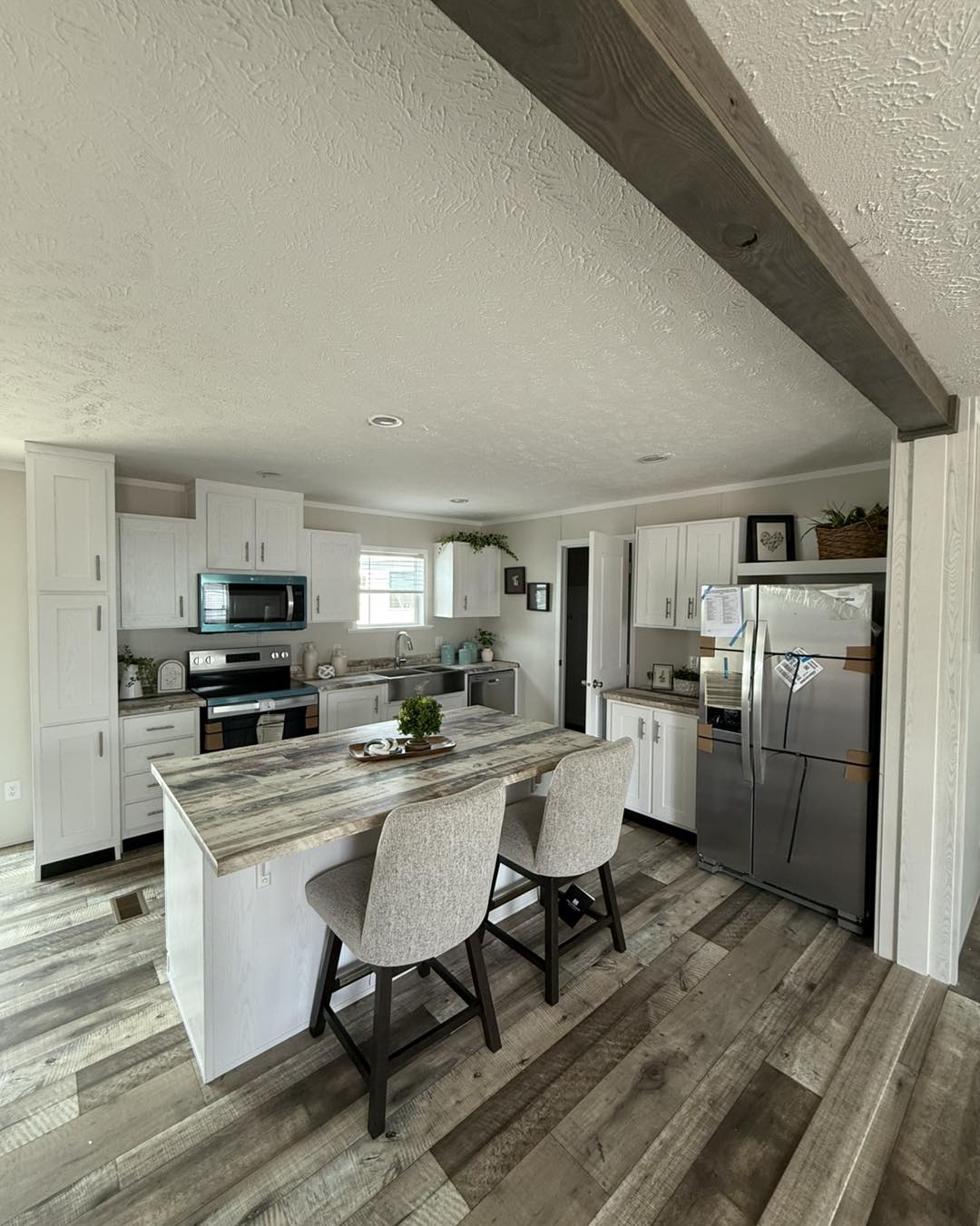 Open-concept living space with light wood flooring, featuring a modern kitchen with white cabinets, a cozy lounge area with a brown sofa, and a round dining table by large windows.