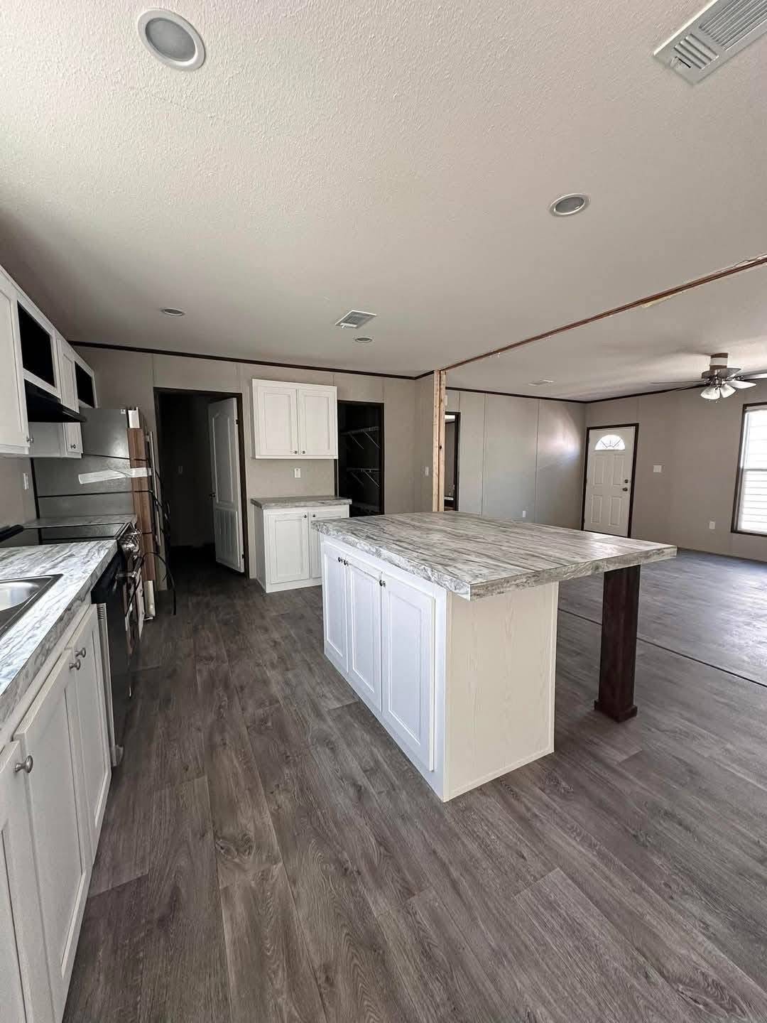 Spacious kitchen with dark wood flooring, a large white island, marble countertops, and stainless steel appliances. Open layout with bright natural light.