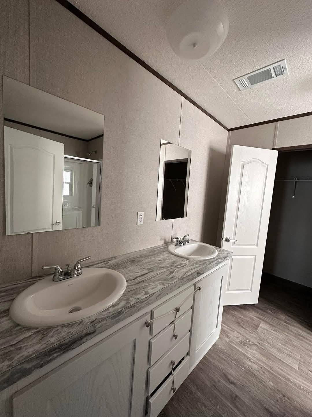 Modern bathroom with dual sinks on a marble countertop, two mirrors above, light gray walls, and a partially open door leading to a closet.