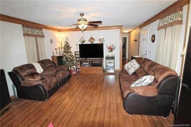 Cozy living room with brown sofas, wood flooring, and a ceiling fan. A decorated Christmas tree stands beside a flat-screen TV on an entertainment unit.