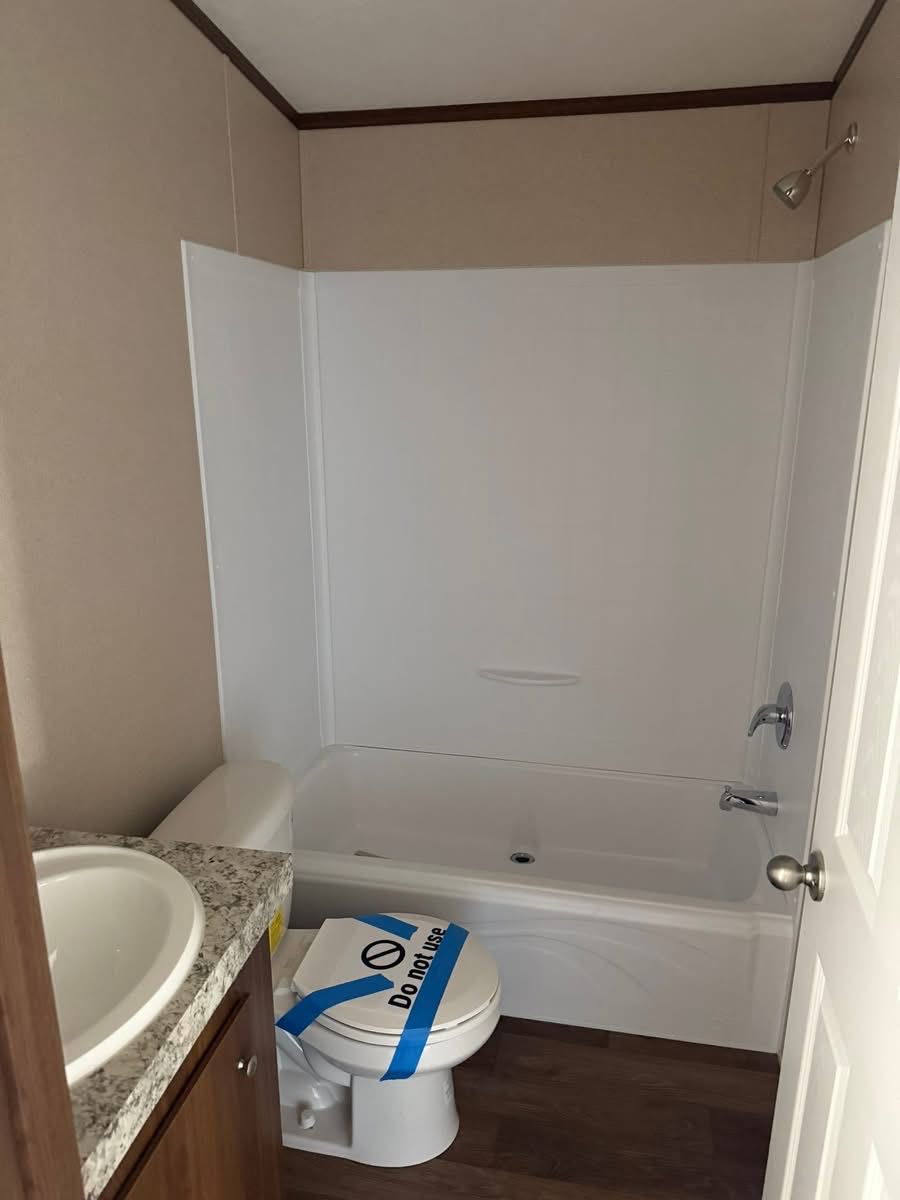 Small bathroom with a tub-shower combo and a toilet with a "Do Not Use" sign and blue tape. A sink with a granite-like countertop is on the left.