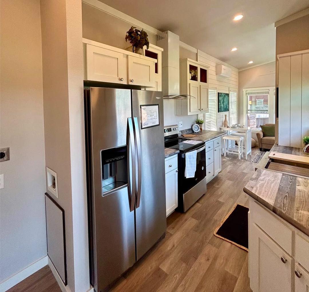 Modern kitchen in a compact home featuring stainless steel appliances, white cabinets, and wood flooring. Bright, inviting, and neatly organized.