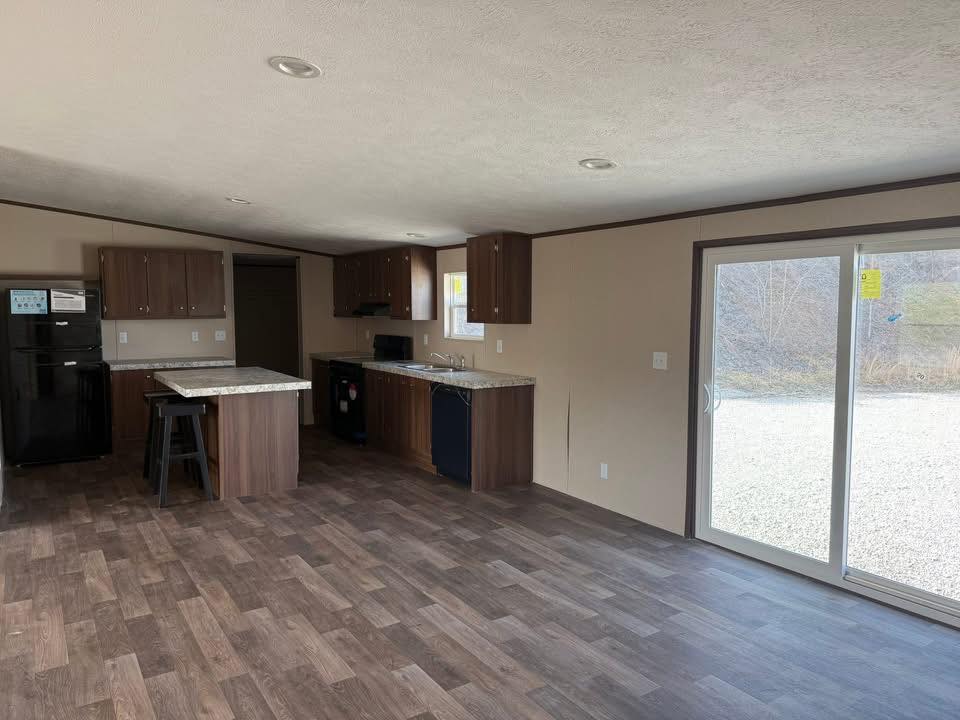 Spacious kitchen with dark wooden cabinets, black appliances, and a marble island. Large sliding glass doors open to the outside, enhancing natural light.
