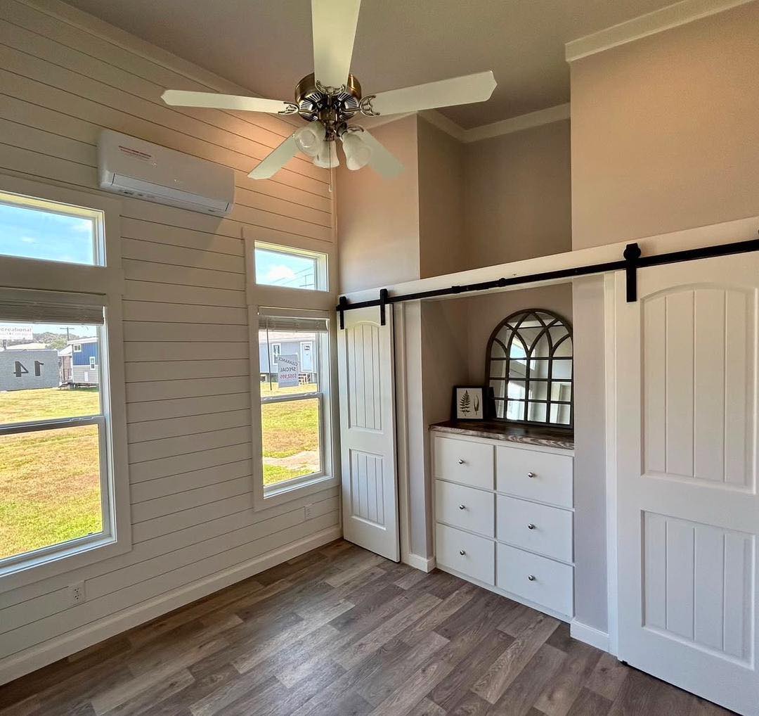 Bright room with wood floors, tall windows, and an elegant ceiling fan. It features a white sliding barn door closet with vintage style decor.