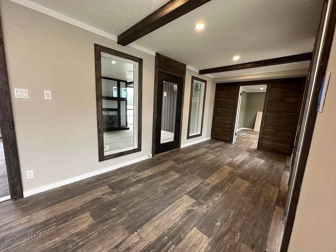 Modern room with dark wood flooring and trim, beige walls, and recessed lighting. Mirrors and windows reflect a bright, clean atmosphere. Cozy and contemporary.