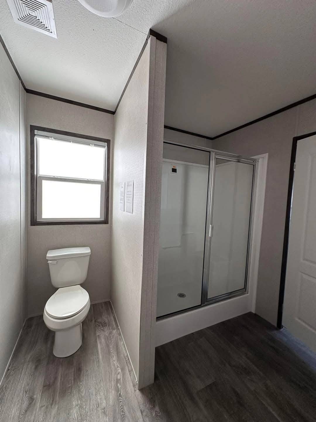 Simple bathroom with a shower stall, sliding glass doors, and a toilet. Light gray walls and wood-style flooring create a clean, minimal look.