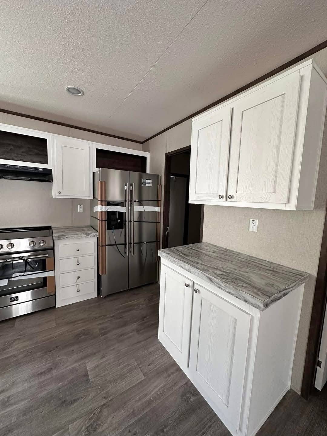 A modern kitchen with sleek stainless steel appliances, white cabinets, and gray countertops. The room features light wood flooring and a neutral wall color, conveying a clean, inviting atmosphere.