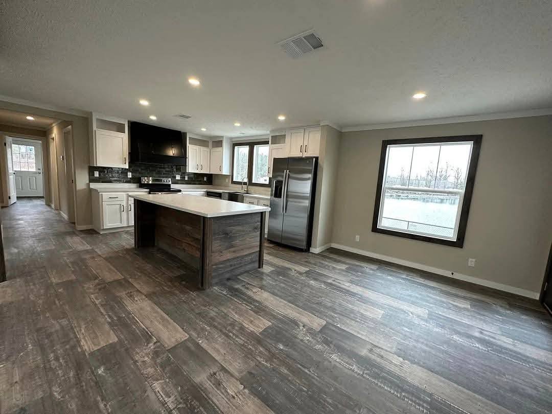 Spacious modern kitchen with a large island, stainless steel appliances, and white cabinets. Wood-look flooring adds warmth, enhanced by natural light.