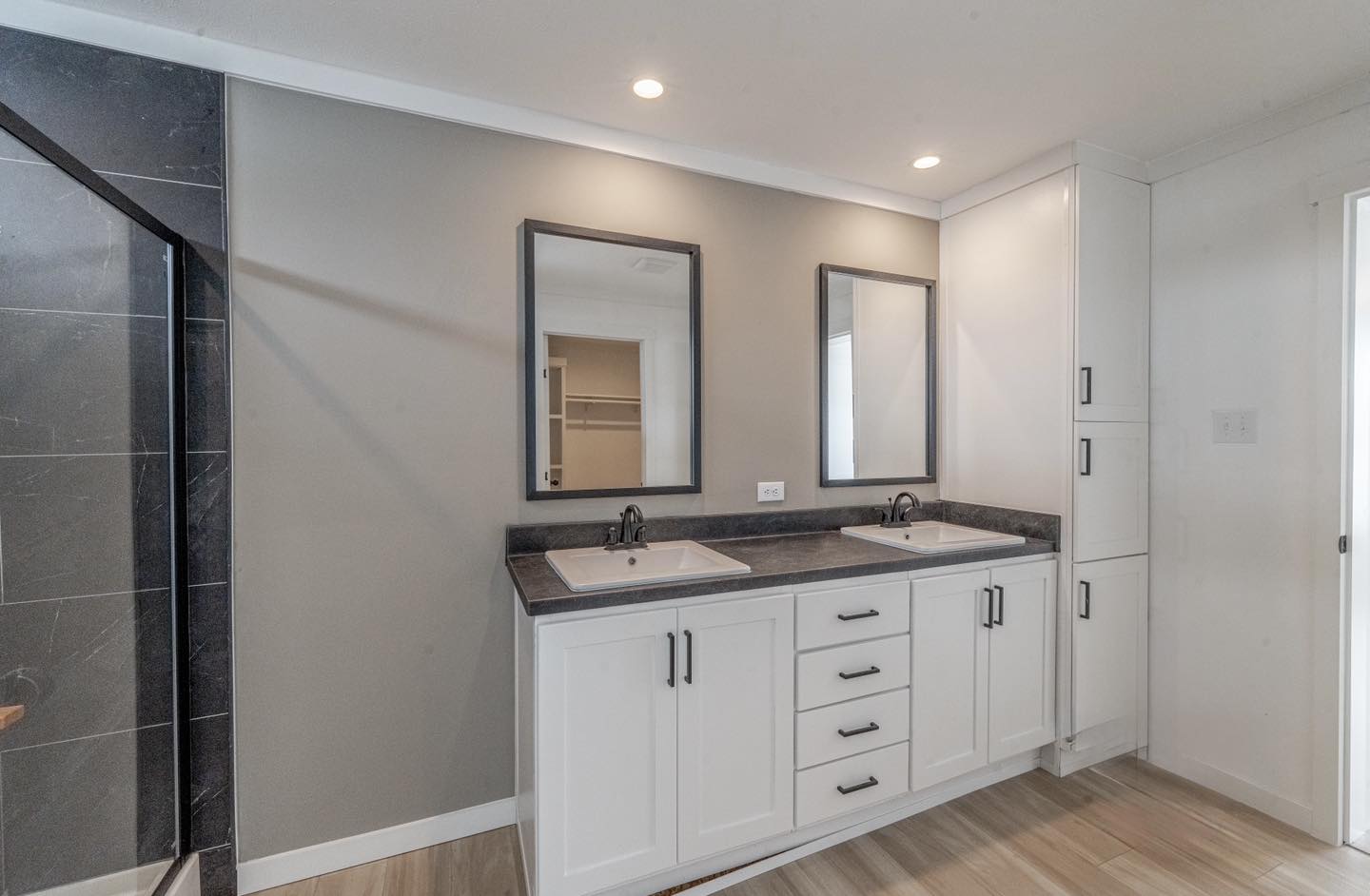 Modern bathroom with dual sinks, white cabinets, and black countertops. Two mirrors hang above the sinks. Neutral tones create a calm ambiance.