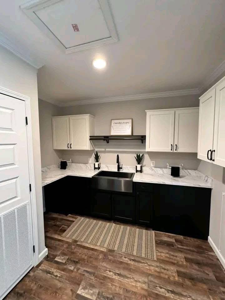 Modern kitchen with a black and white theme, featuring white upper cabinets, dark lower cabinets, a farmhouse sink, and a striped rug on wood floors.