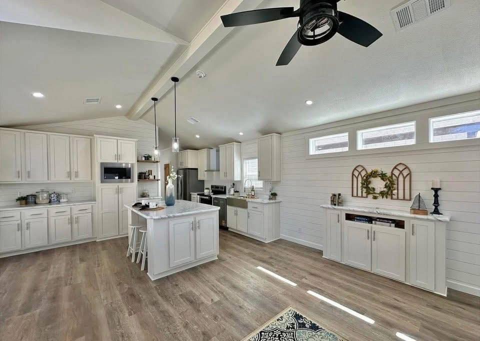 Spacious modern kitchen with white cabinets, a central island, and wood flooring. Ceiling fan and pendant lights create a warm, inviting atmosphere.