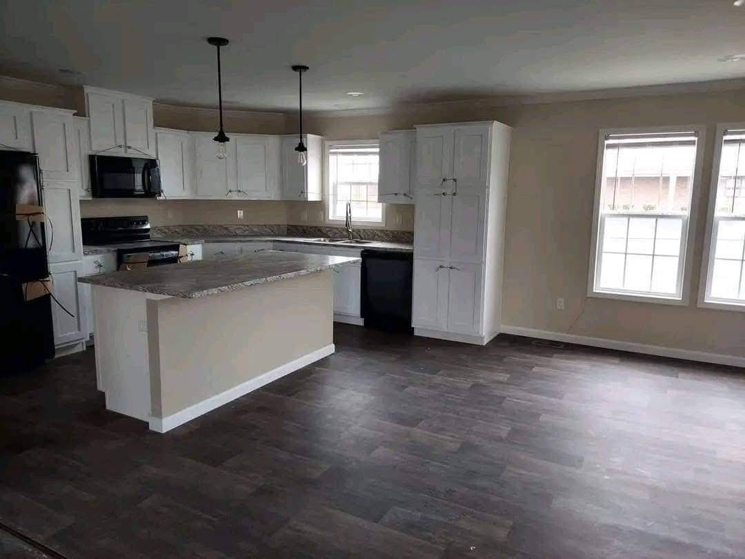 Spacious kitchen with dark wood floors, white cabinets, and a granite-topped island. Black appliances and pendant lights create a modern feel.