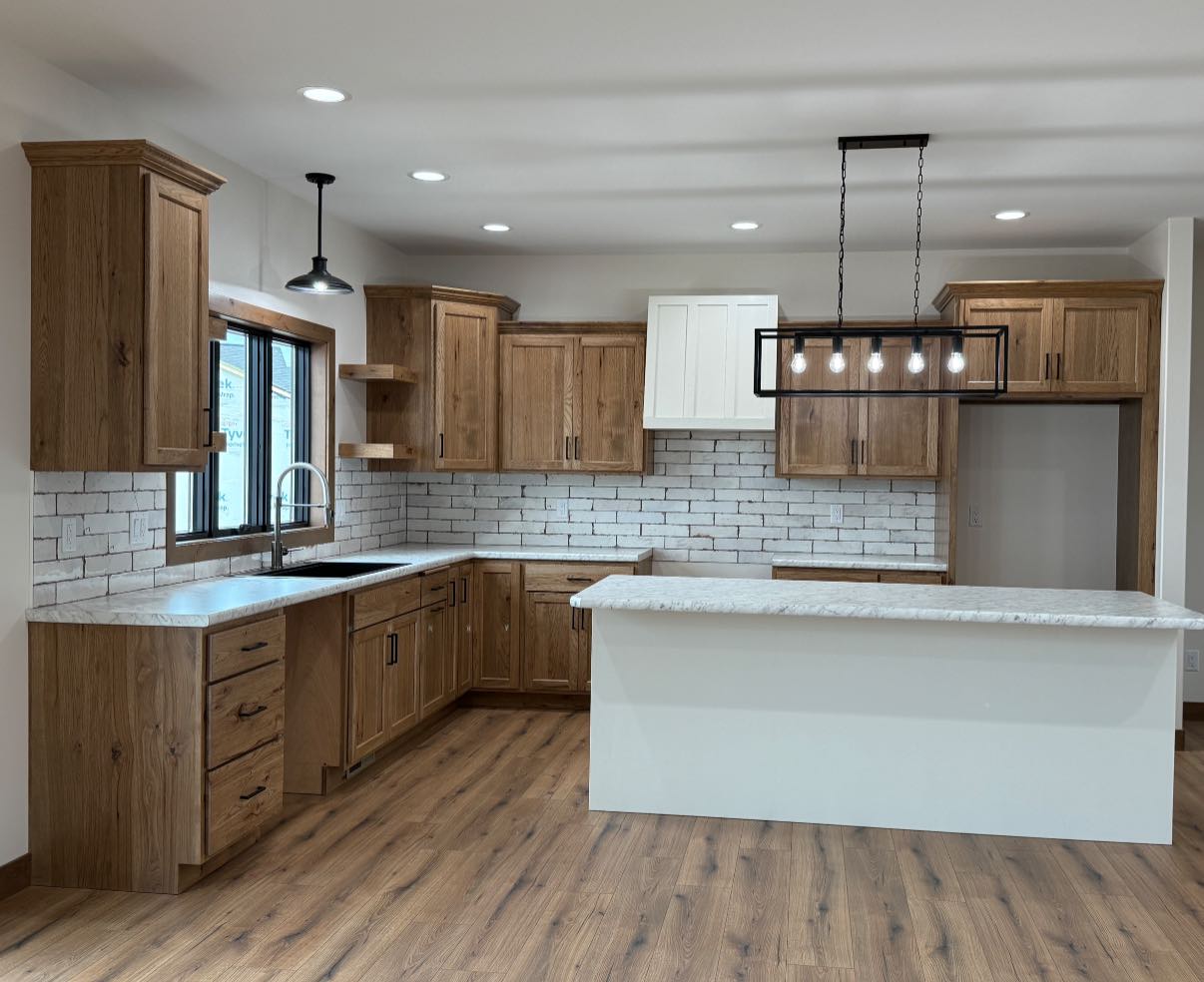 Spacious kitchen with wood cabinets, white brick backsplash, and a large island. Modern pendant light hangs above, creating a warm, inviting feel.