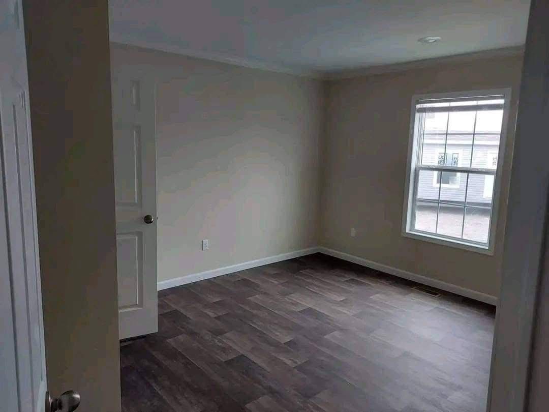 Empty room with light gray walls, dark wood flooring, a white door slightly ajar, and a large window letting in soft natural light. Minimalist and calm.