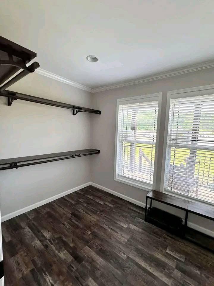 Small, bright room with hardwood flooring and two large windows with blinds. Dark wooden shelves and a bench give a clean, minimalist look.